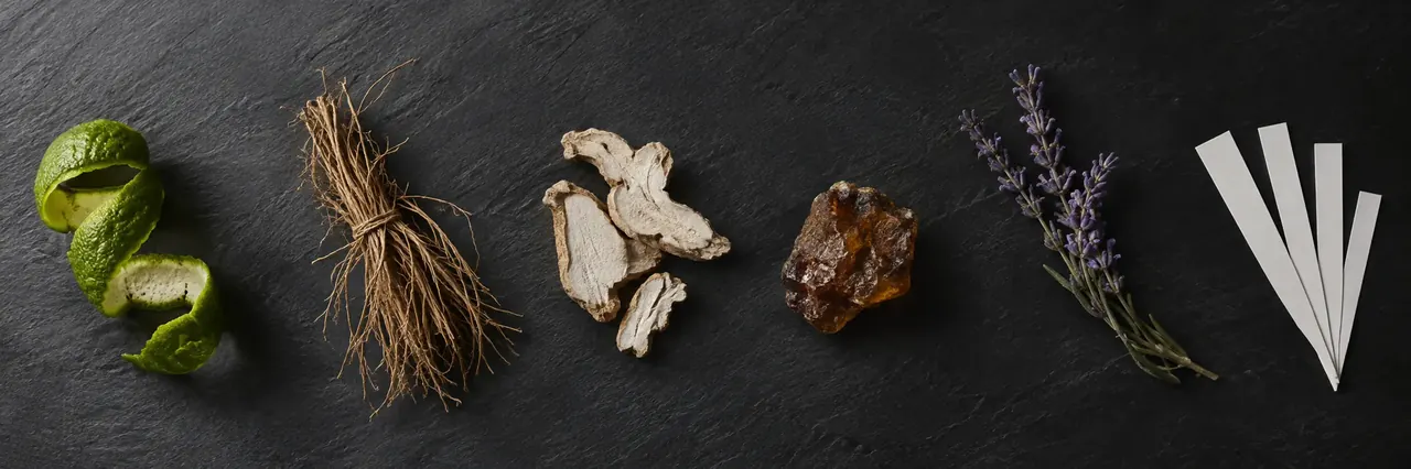 Matières premières de parfumerie sur ardoise : zestes d’agrumes, racines de vétiver, racine d’iris, résine de labdanum, lavande et mouillettes.